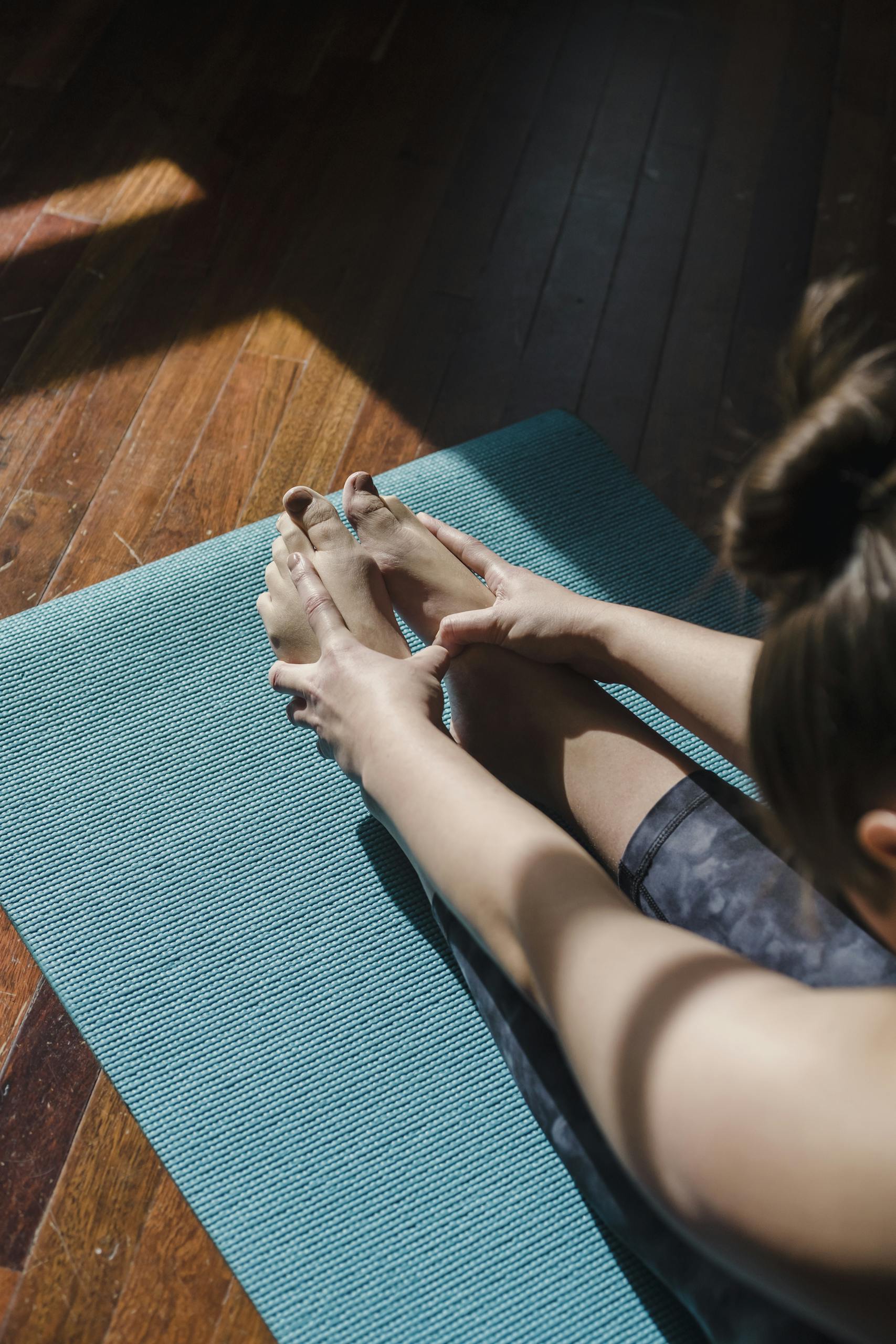 Pilates 1 A woman performs a yoga stretch on a blue mat indoors, emphasizing flexibility and wellness.