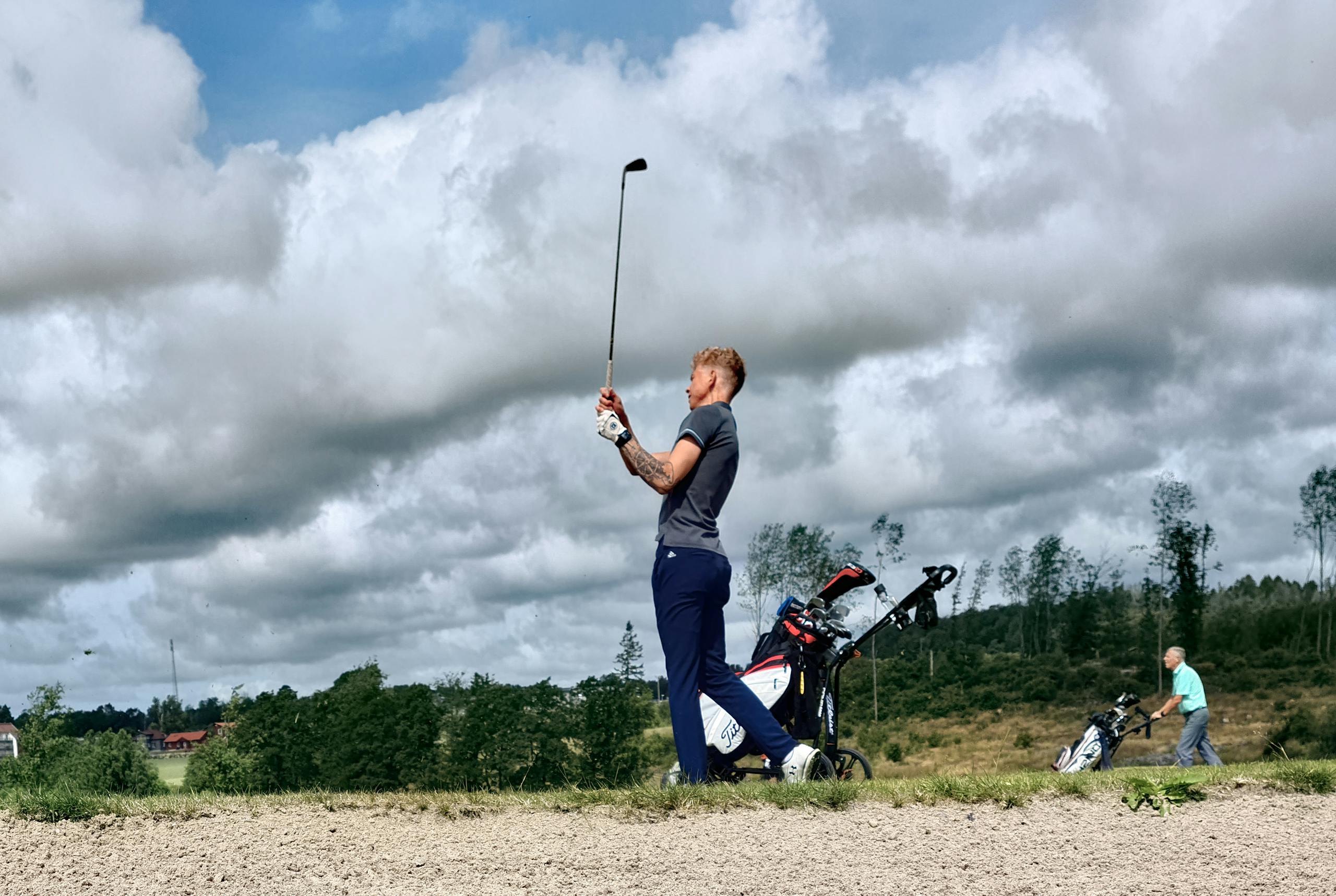 Two golfers playing on a lush outdoor course in Halland, Sweden, under a cloudy sky.